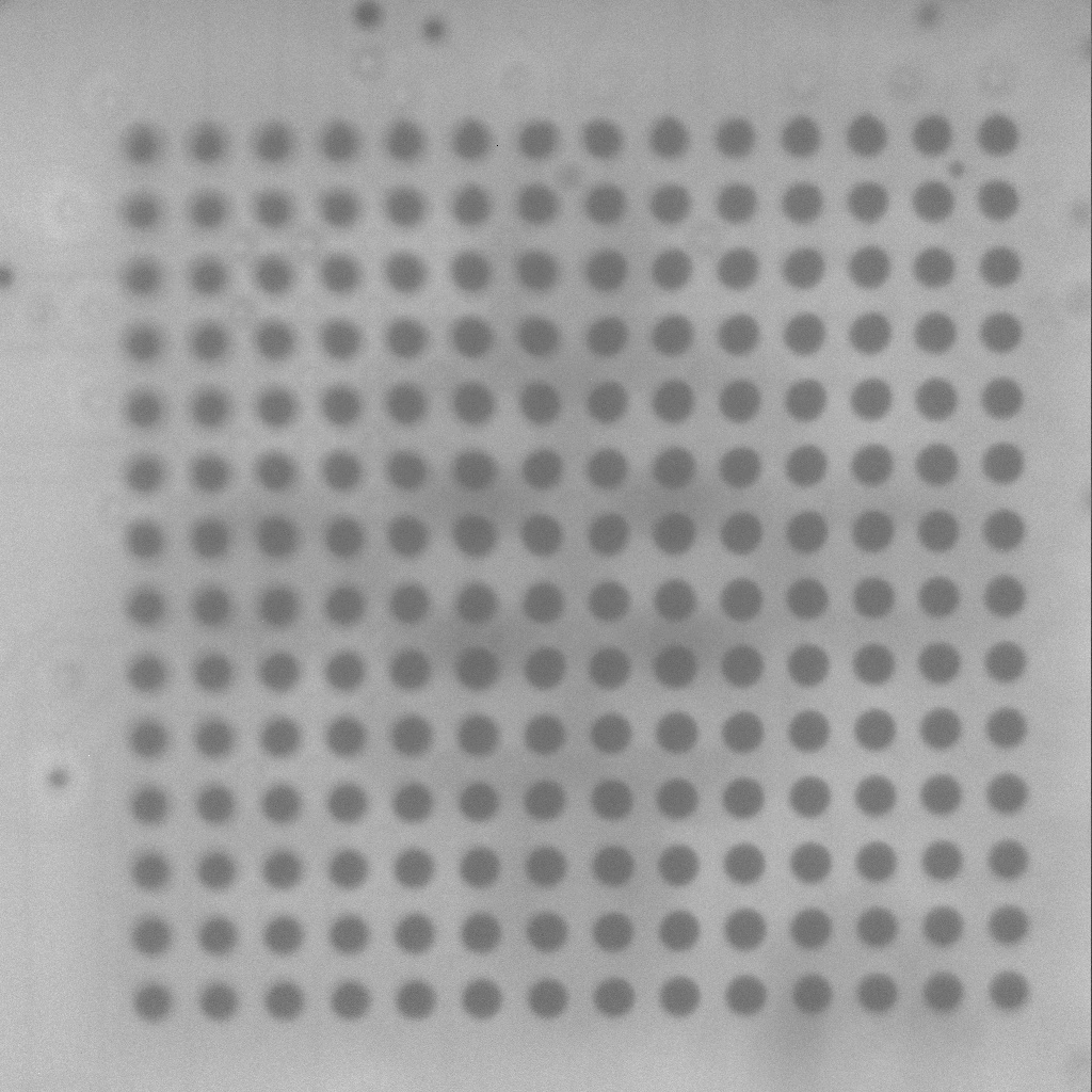 X-ray image of a 14 by 14 ball BGA chip on a printed circuit board, viewed from above. The image reveals the regular grid of solder ball joints between the chip and the PCB as small dark circles, allowing inspection of joint integrity without removing the chip. A few of the solder joints are visibly asymmetric or partially formed, which would be flagged as defects in a manufacturing context. Forensic labs use the same kind of X-ray imaging to verify joint integrity after rework, to confirm a chip has been seated correctly in its socket adapter, and as part of the documentation record for invasive acquisition.