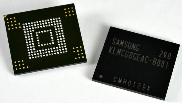 Photograph of a Samsung KLMCG8GEAC eMMC memory chip removed from a circuit board, viewed from the underside to show the BGA solder ball pattern. The chip is roughly square with a uniform grid of small round solder balls covering most of the underside surface. A subset of these balls correspond to the standardized eMMC interface signals (CMD, CLK, DAT0 through DAT7, VCC, VCCQ, and GND) that an ISP examiner solders to in order to read the chip in place.